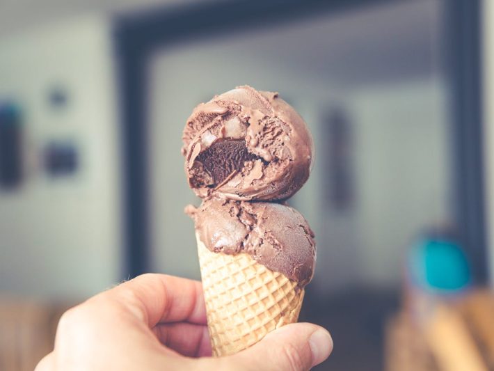 A person holding a cone of chocolate ice cream